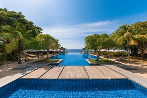 A clear view of a swimming pool with a wooden deck, surrounded by palm trees and lounge chairs. - Crimson Resort and Spa Mactan (Lapu-Lapu)