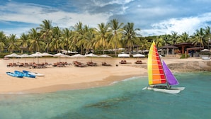 A beach with clear turquoise water, palm trees, and a sailboat with a colorful sail. - Crimson Resort and Spa Mactan (Lapu-Lapu)