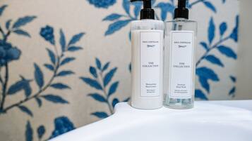 Two Paul Costello The Collection hand wash bottles on a white surface with a floral patterned background.