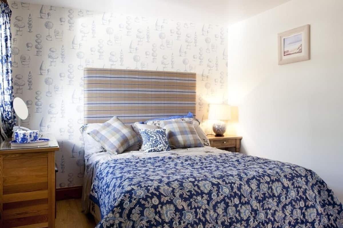 A bedroom with a striped headboard, a bed with patterned bedding, a bedside table with a lamp, and a dresser.