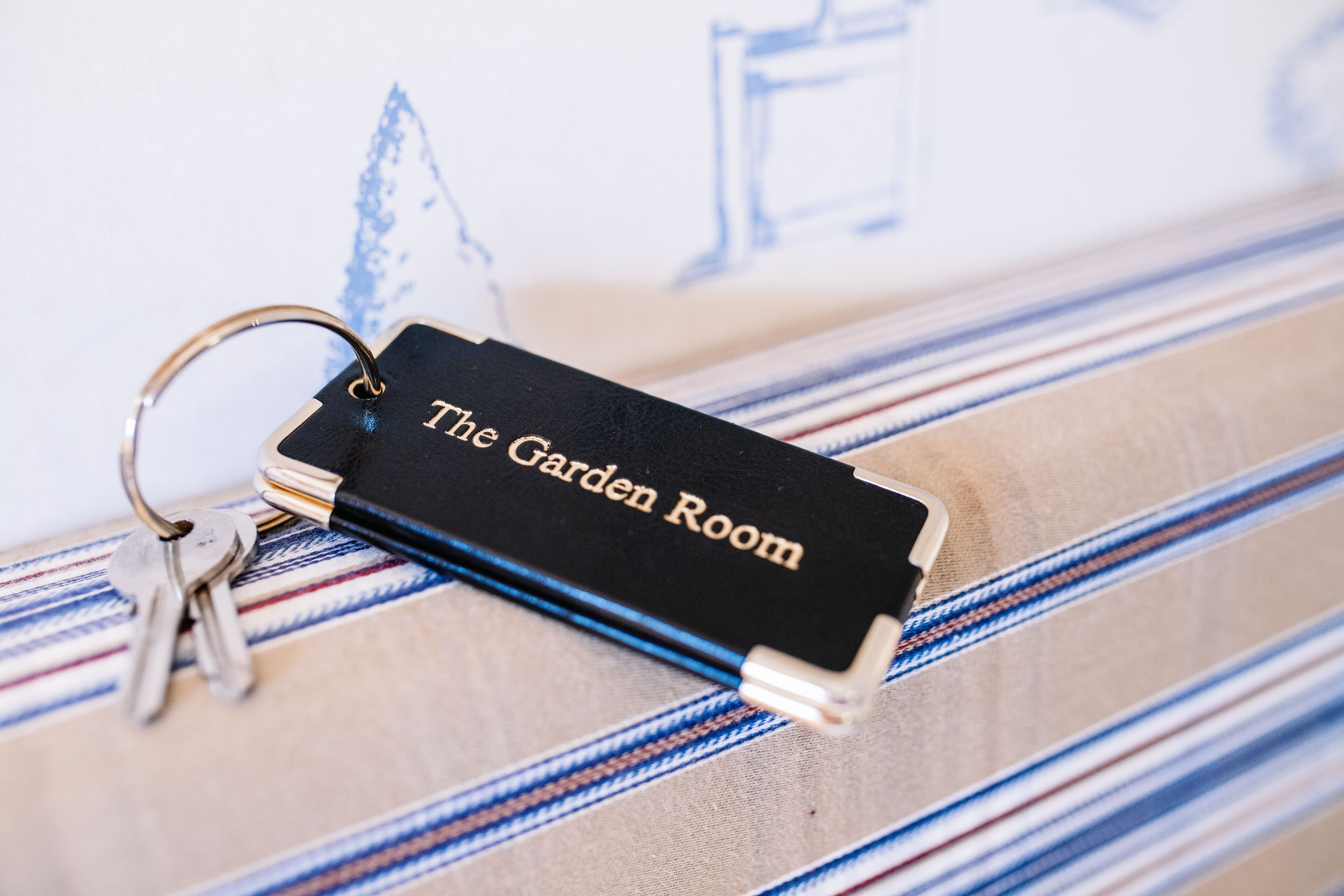 Un porte-clés avec la mention « The Garden Room » gravée, posé sur une surface en tissu à rayures.