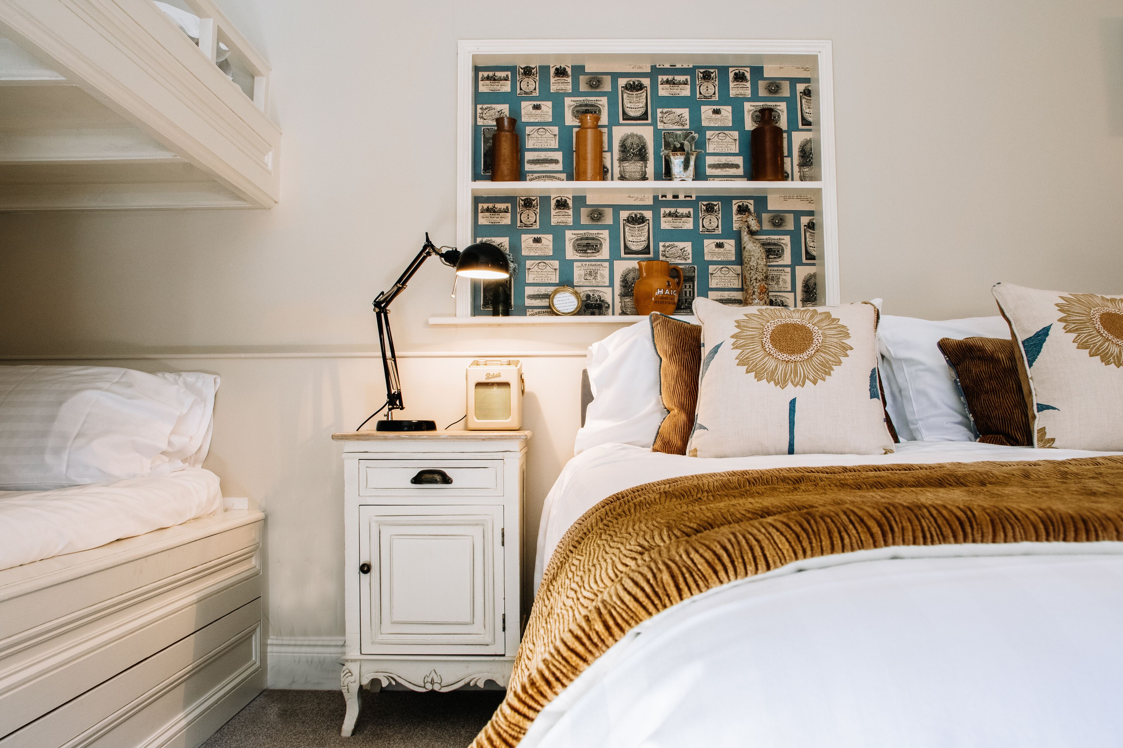 Een slaapkamer met een bed, een nachtkastje, een plank met decoratieve objecten, en een wand met ingelijste foto's.