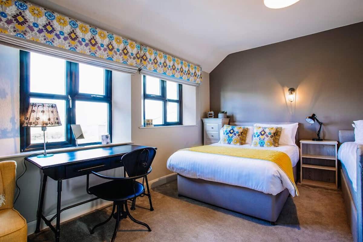 A bedroom with a bed, desk, chair, and bedside table.