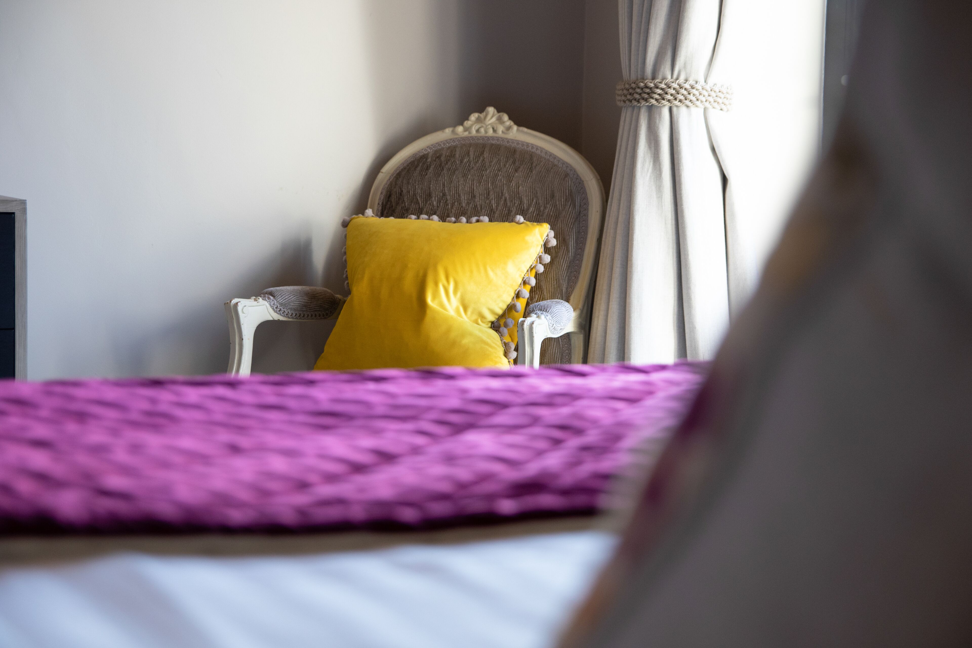 Una cama con un edredón morado, una almohada amarilla y un cabecero blanco.