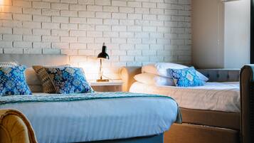 A hotel room with a brick wall, two beds with patterned bedding, a nightstand with a lamp, and a chair.