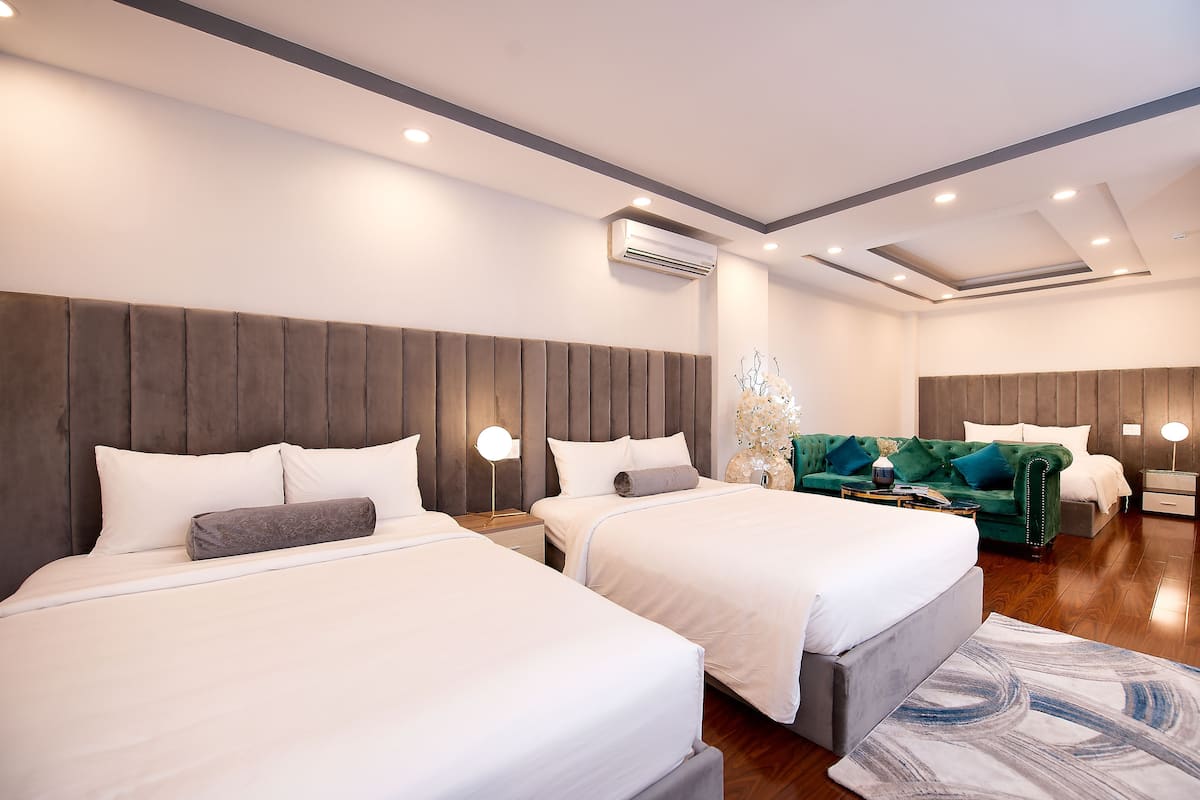 Une chambre d’hôtel moderne avec deux lits, un canapé vert et une grande fenêtre.