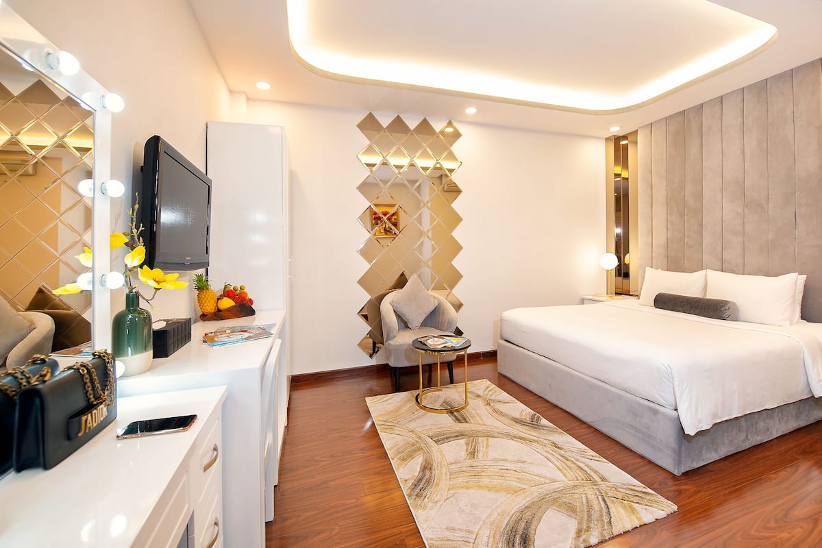 Une chambre à coucher moderne comprenant un lit, une table de chevet, une coiffeuse avec miroir et éclairage, et un panneau décoratif mural.