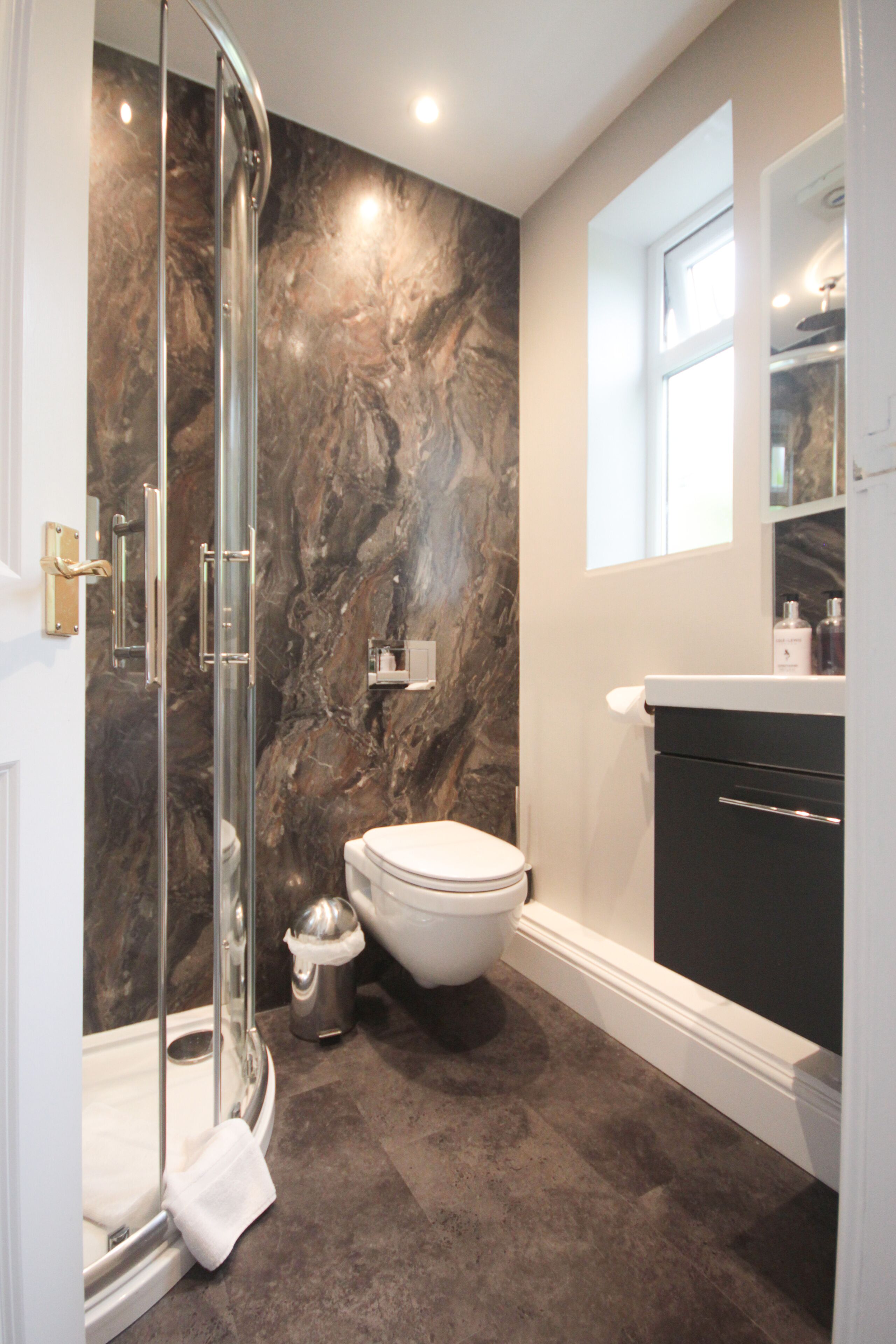 A bathroom with a glass-enclosed shower, a white toilet, and a dark marble wall.