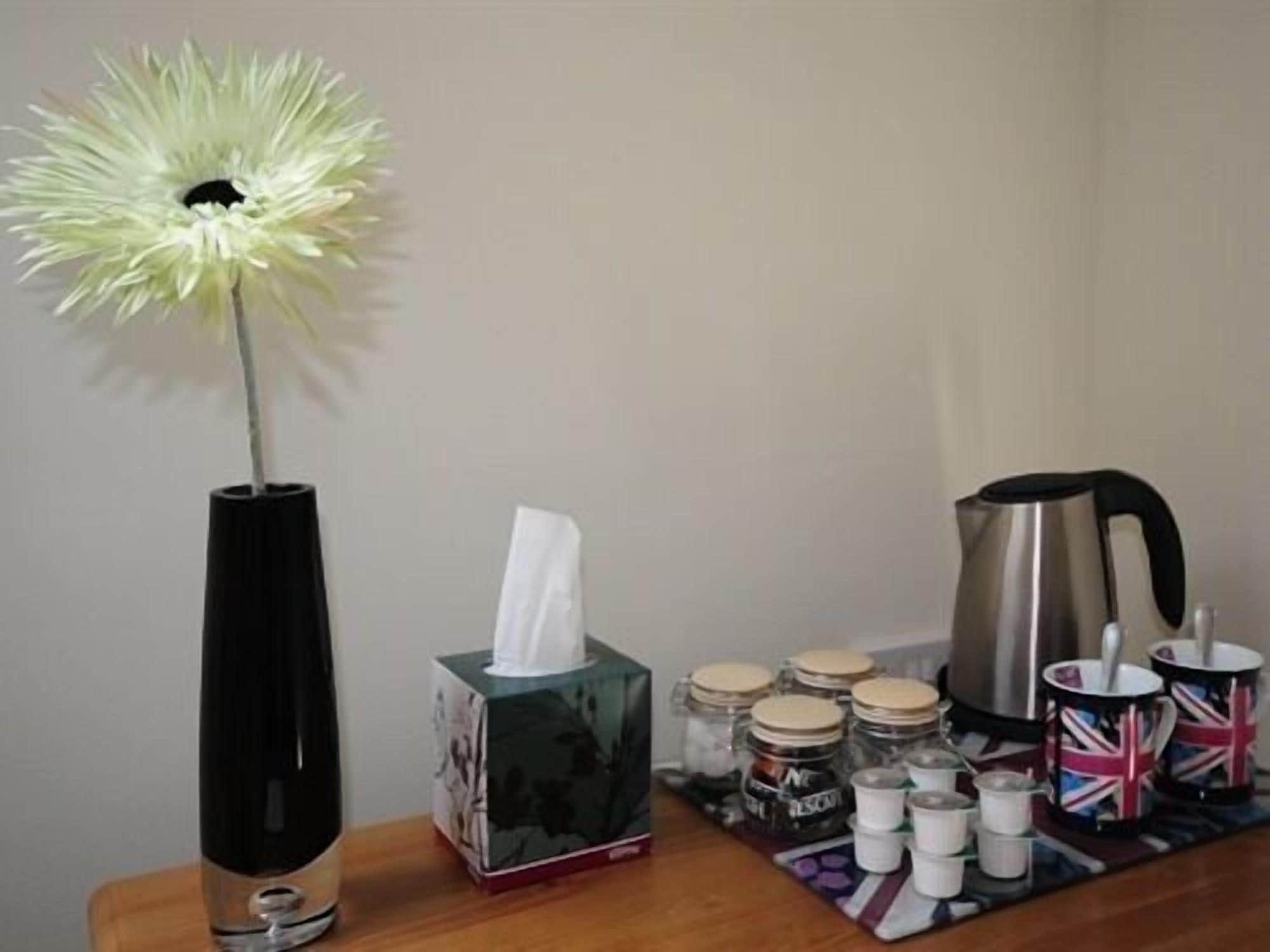 Une table avec un vase, une boîte de mouchoirs, des bocaux, une bouilloire et des tasses.