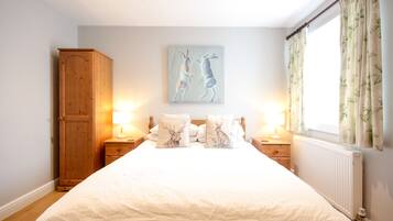 A bedroom with a large bed, two bedside tables with lamps, a wooden wardrobe, and a painting of deer on the wall.