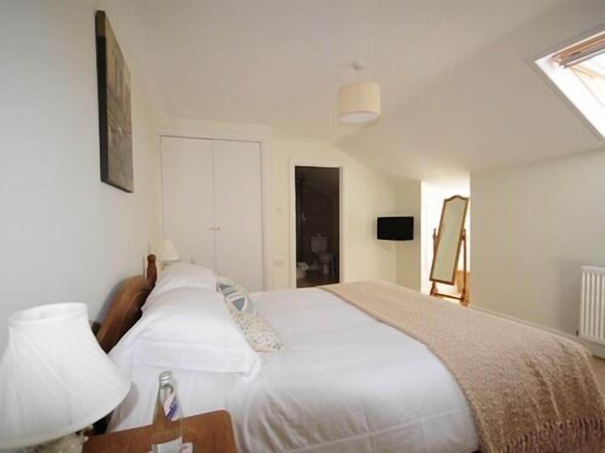 A bedroom with a bed, a bedside lamp, a painting on the wall, a door, and a window.