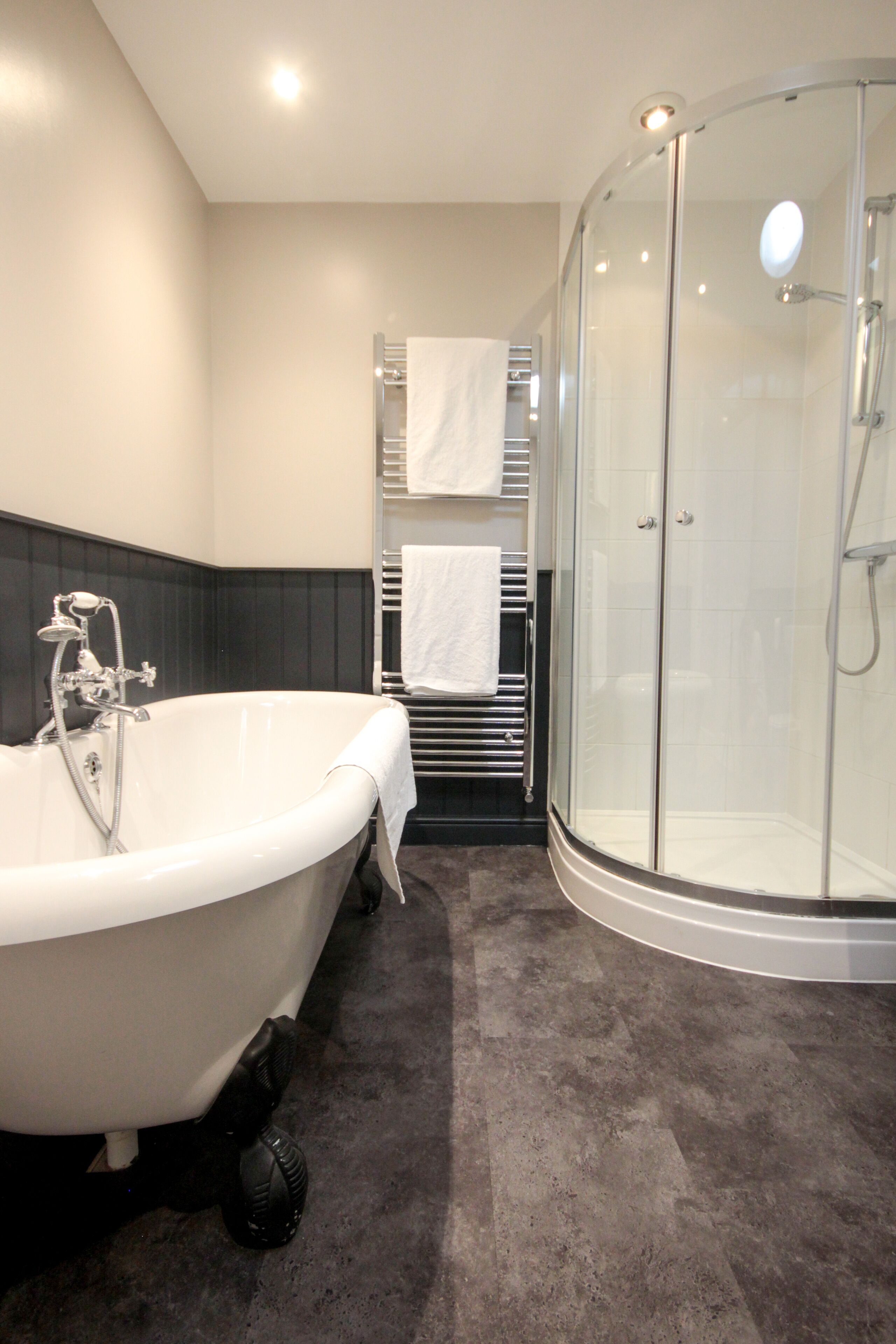 A modern bathroom with a freestanding bathtub, a glass-enclosed shower, and a towel rack with white towels.