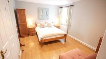 A bedroom with a wooden bed, bedside tables, a wardrobe, and a window with curtains.