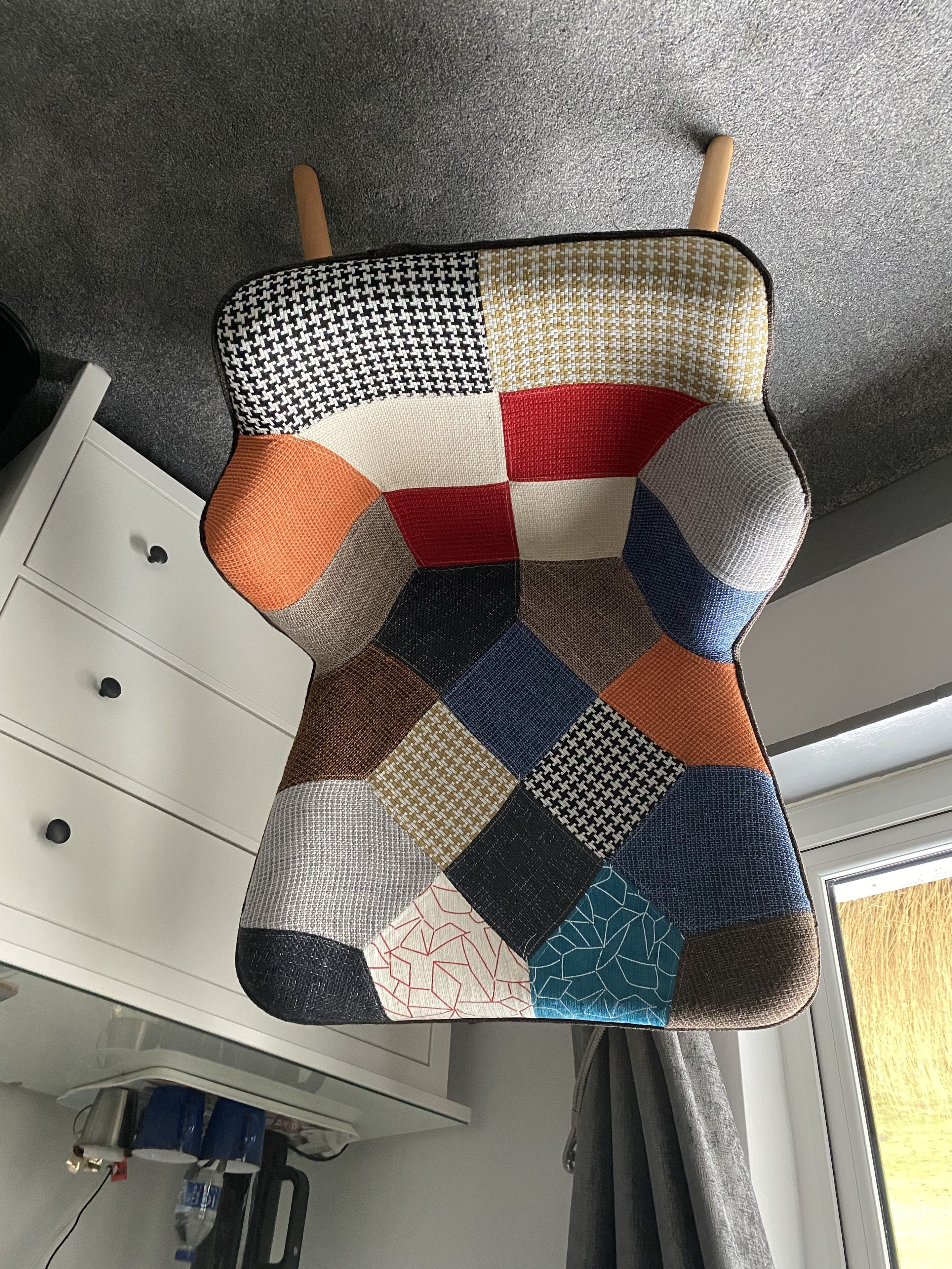 Uma cadeira acolchoada com design em patchwork, um penteou branco e uma janela com cortinas.