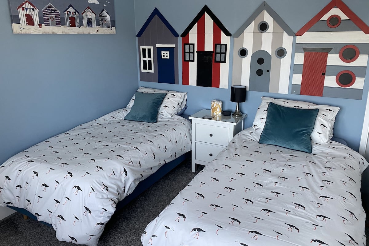 Ein Schlafzimmer mit zwei Betten, einem Nachttisch und einer Wand mit einem Kunstwerk zum Thema Strand.