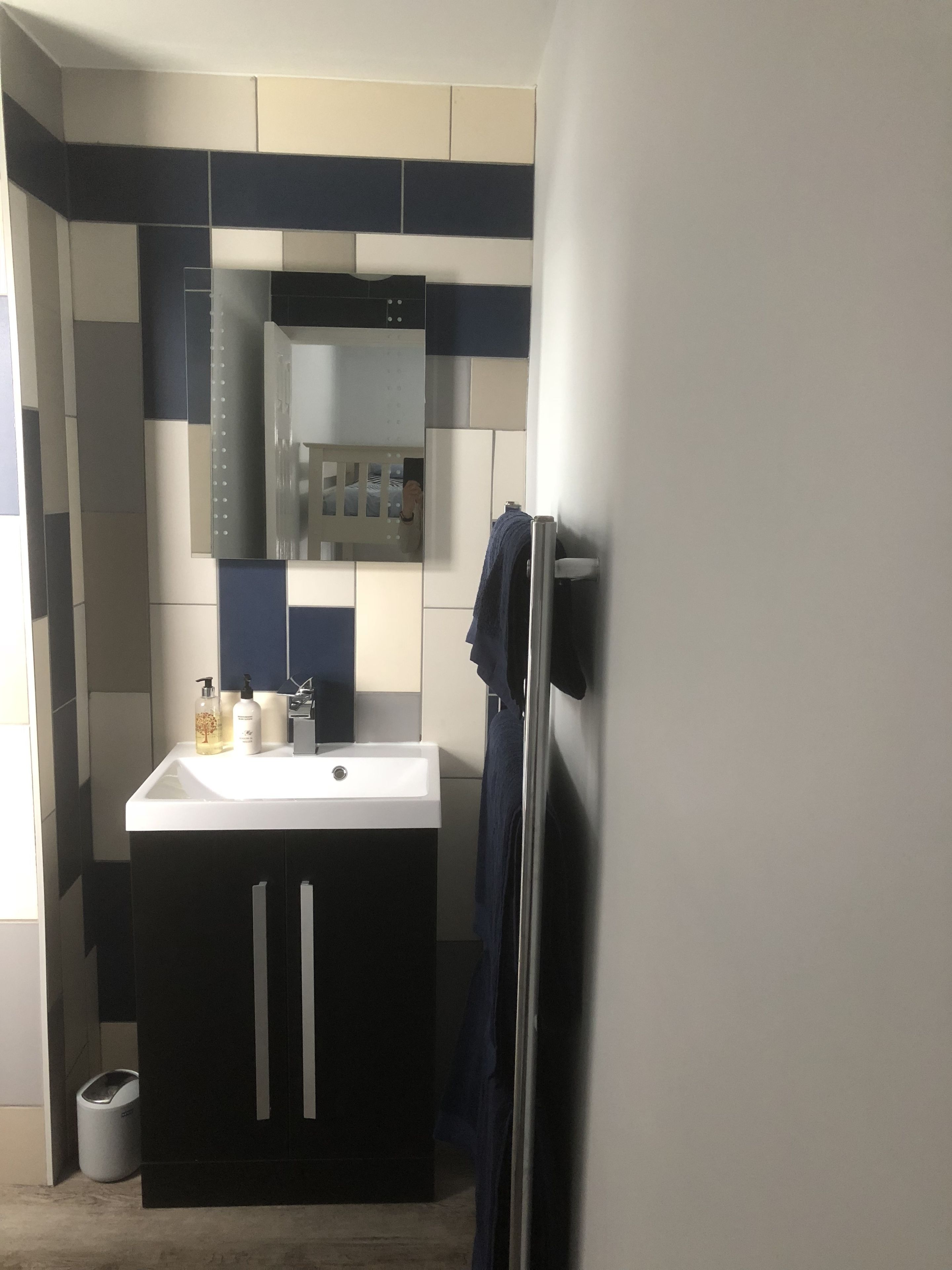 Une salle de bain avec un lavabo blanc, des meubles sombres et un miroir au-dessus.