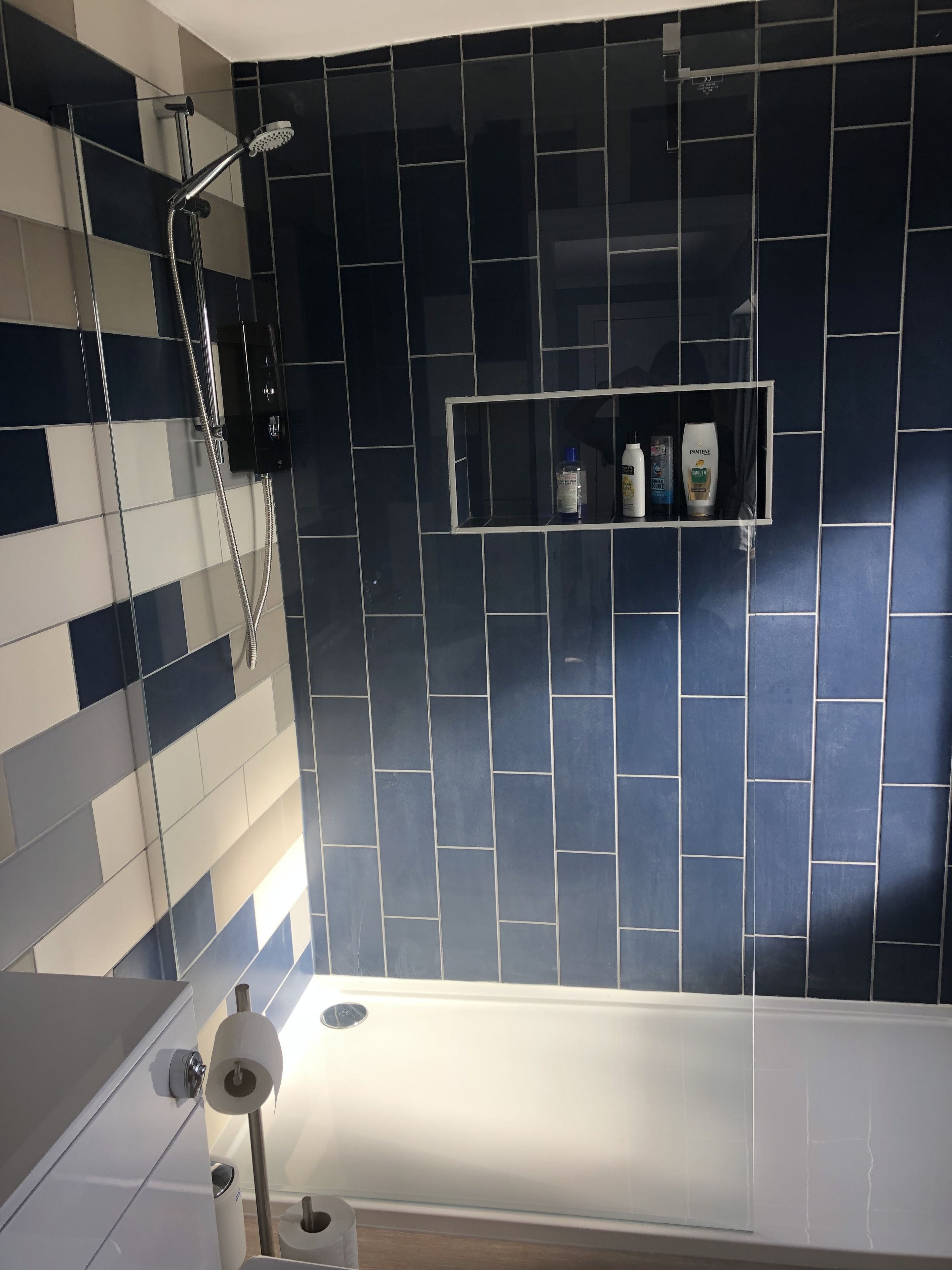 Et badeværelse med bruser, toilet og en hylde med toiletartikler.