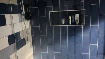 Un baño con ducha, inodoro y un estante con artículos de aseo.