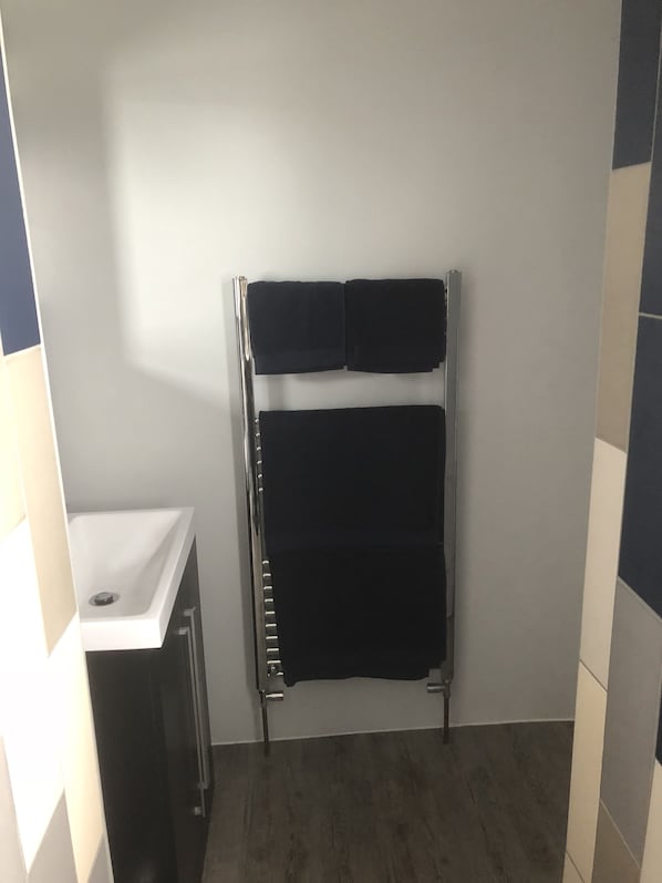 Un baño pequeño con un lavamanos blanco, un toallero con dos toallas y suelo de madera.