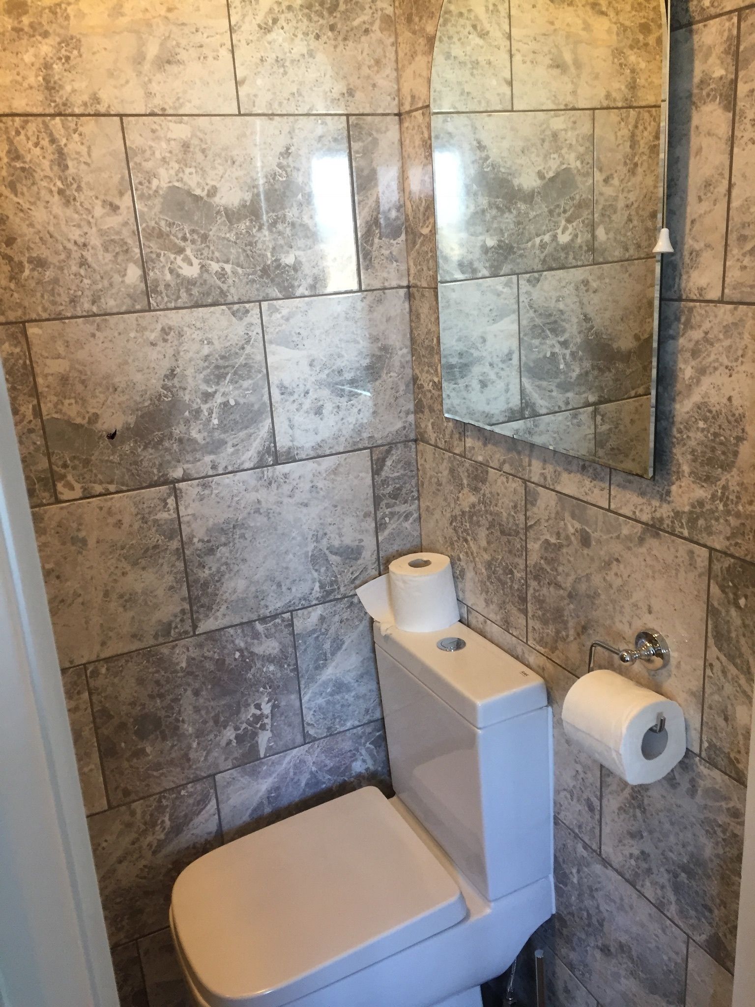 Un baño con inodoro, espejo y dispensador de papel higiénico.
