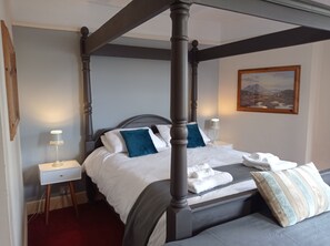 A four-poster bed with white linens and blue pillows, a bedside table with a lamp, and a painting on the wall. - The Castle Hotel (Hythe)