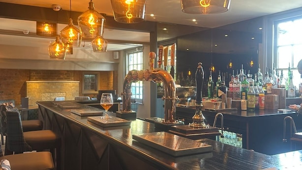 A bar area with multiple hanging light fixtures, a bar counter, and a seating area with chairs. - The Boot Inn (Worcester)