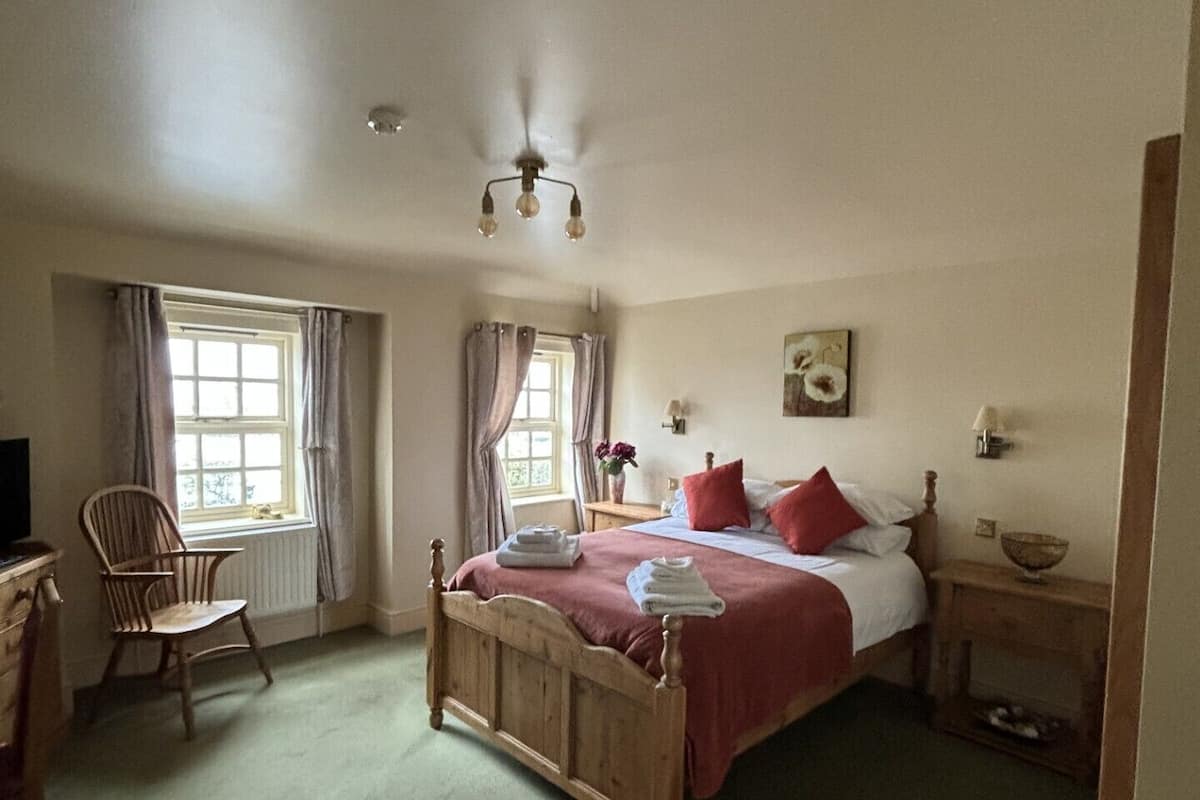 A bedroom with a wooden bed, a chair, a nightstand, and a window with curtains.