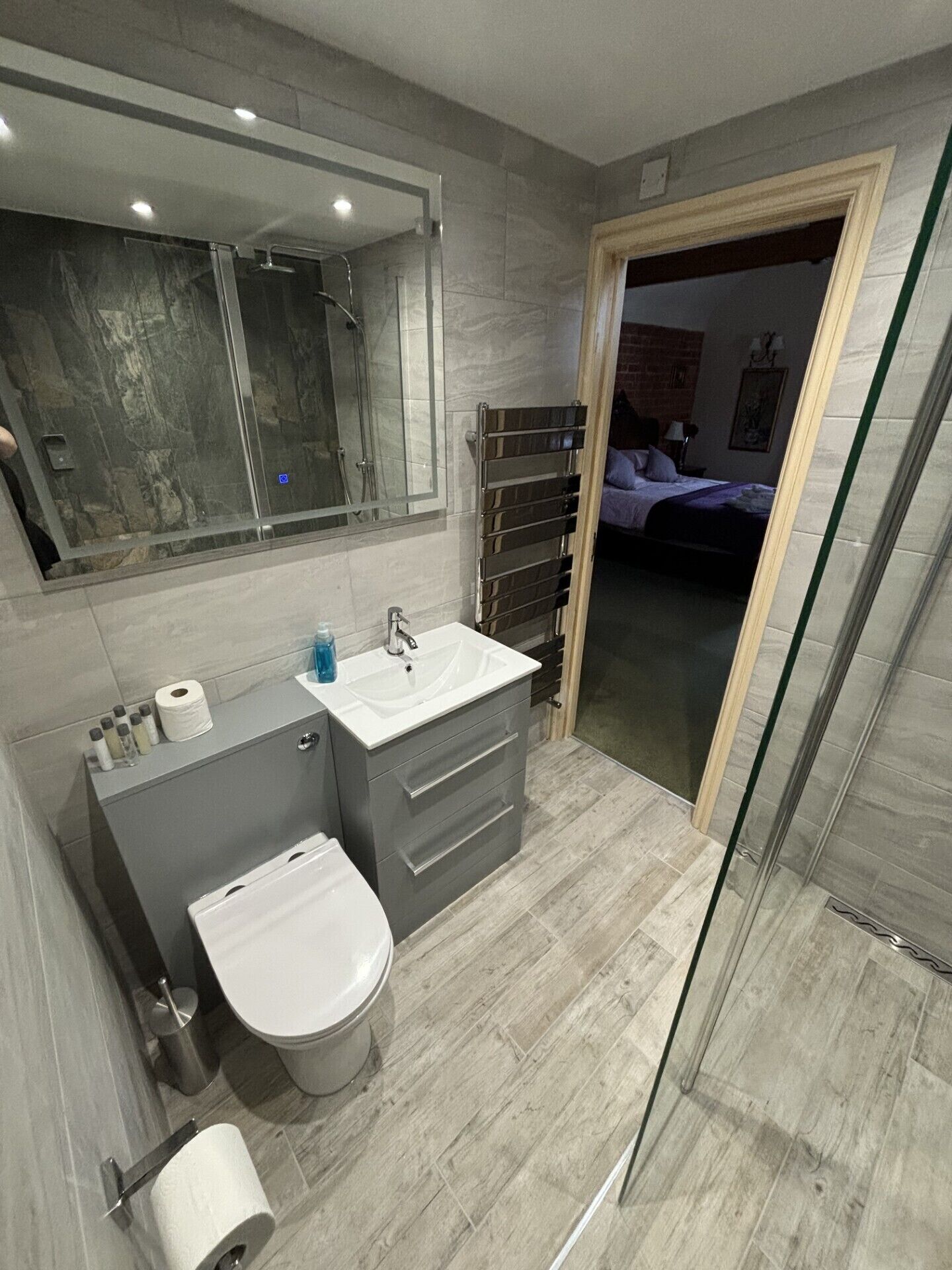 Un bany modern amb plat de dutxa de vidre, un lavabo amb rentapans i mirall, i un vàter.