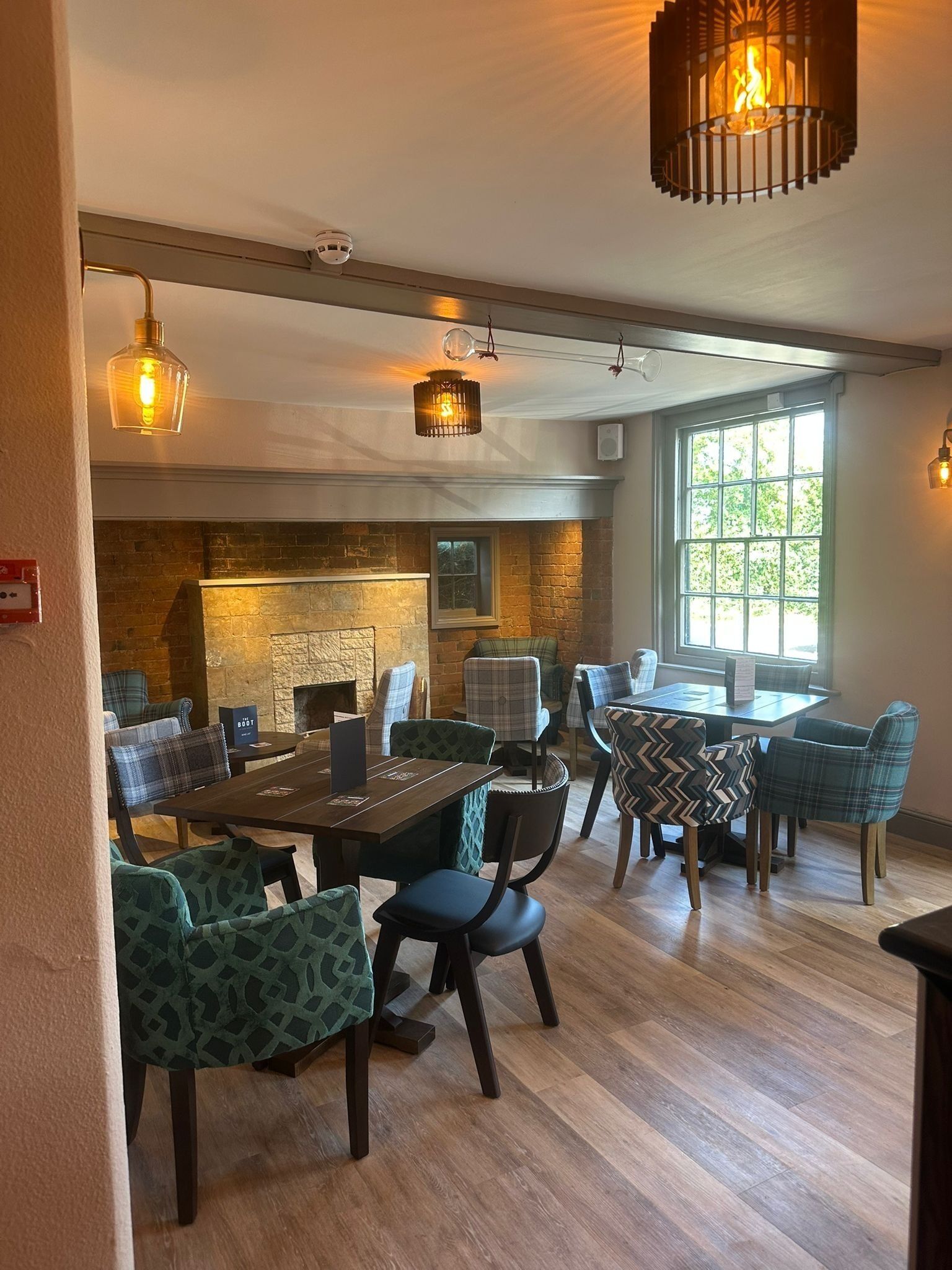 Een gezellig restaurant met een metselwerk open haard, houten tafels en stoelen met ruitdessin.