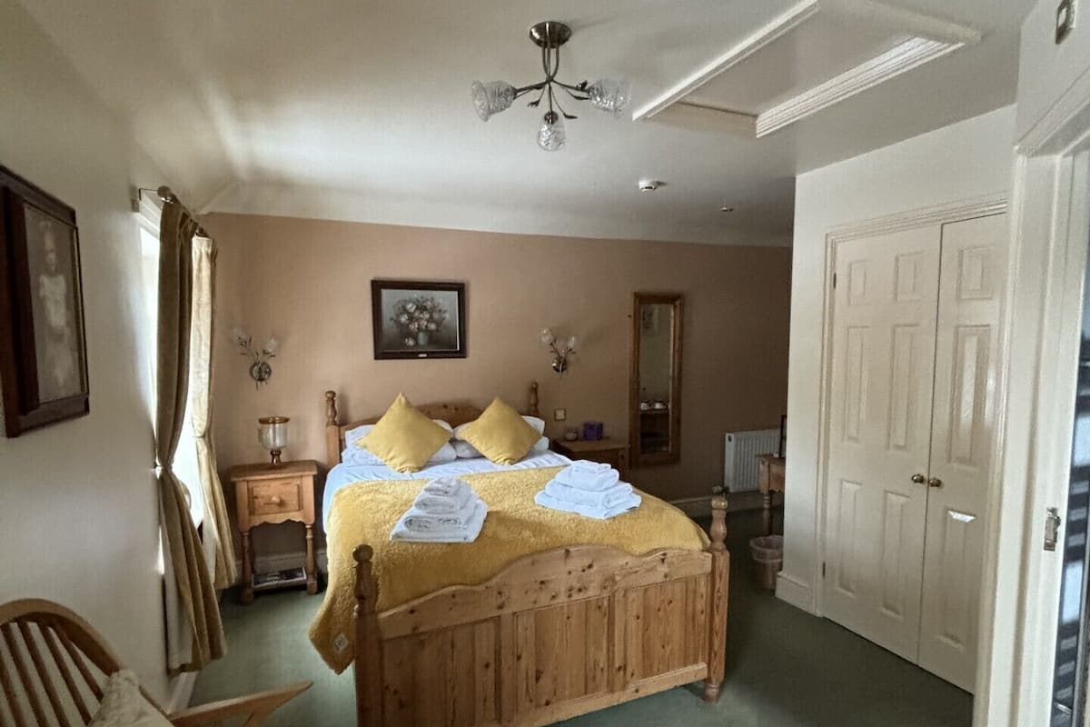 A bedroom with a wooden bed, a chair, a nightstand, a mirror, and a wardrobe.