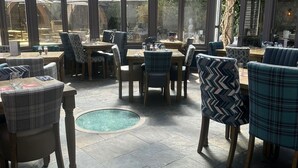 A conservatory with a glass ceiling, furnished with tables and chairs, and a small pool. - The Boot Inn (Worcester)