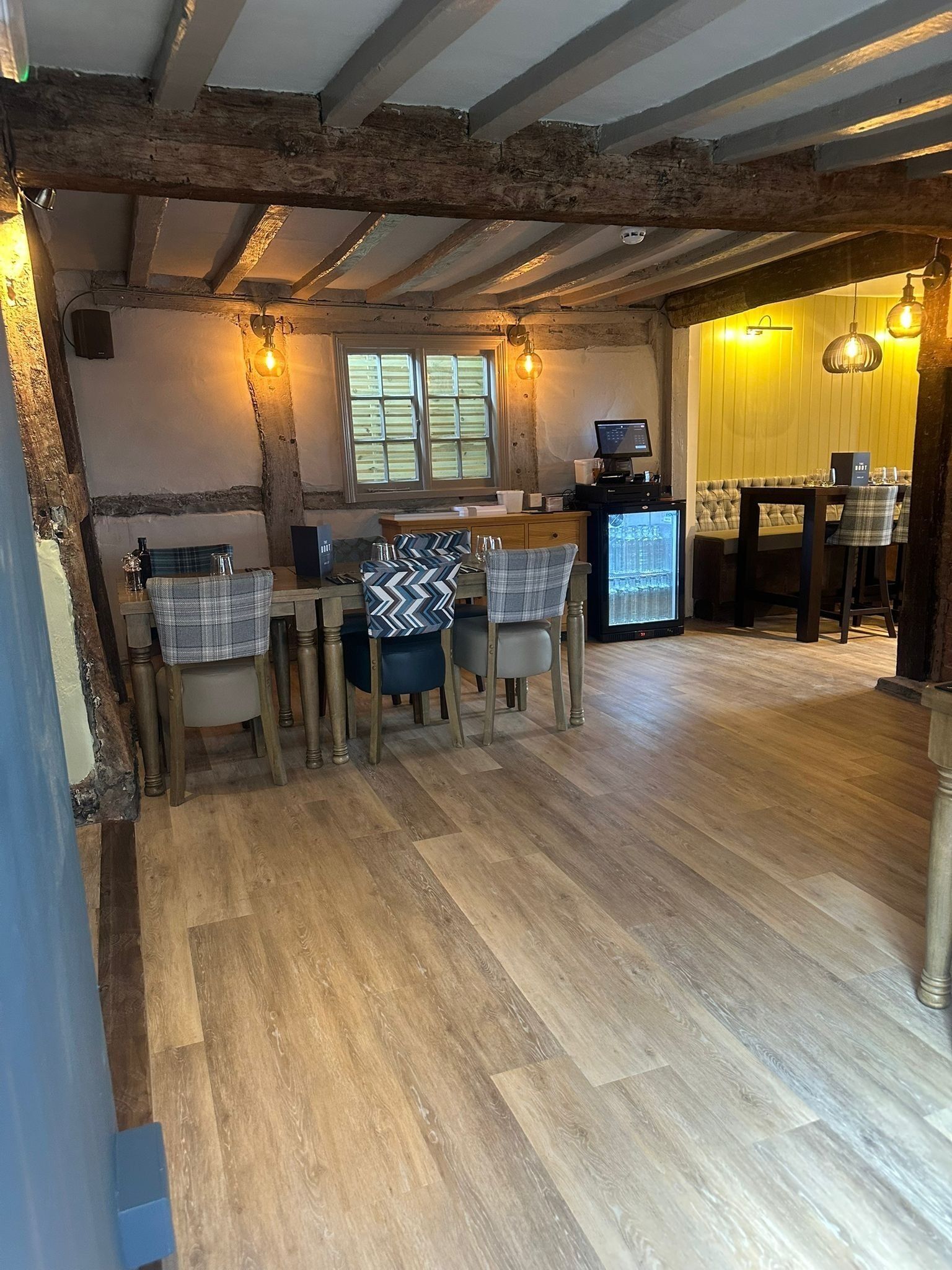 A rustic dining area with exposed wooden beams, a wooden table with chairs, and a television on a stand.