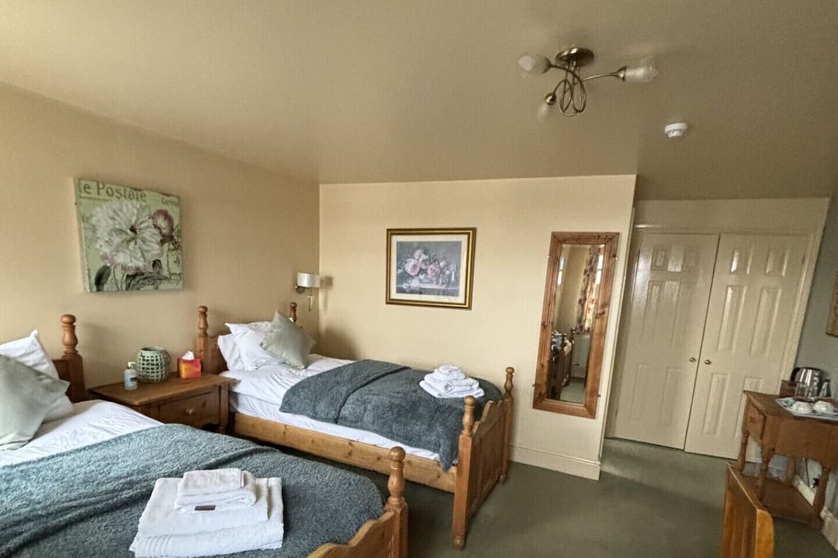 A room with two wooden beds, a small table, a chair, a mirror, and a wardrobe.