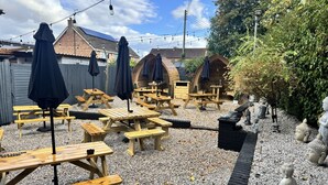 An outdoor seating area with wooden picnic tables and umbrellas, surrounded by gravel and decorative statues. - The Boot Inn (Worcester)
