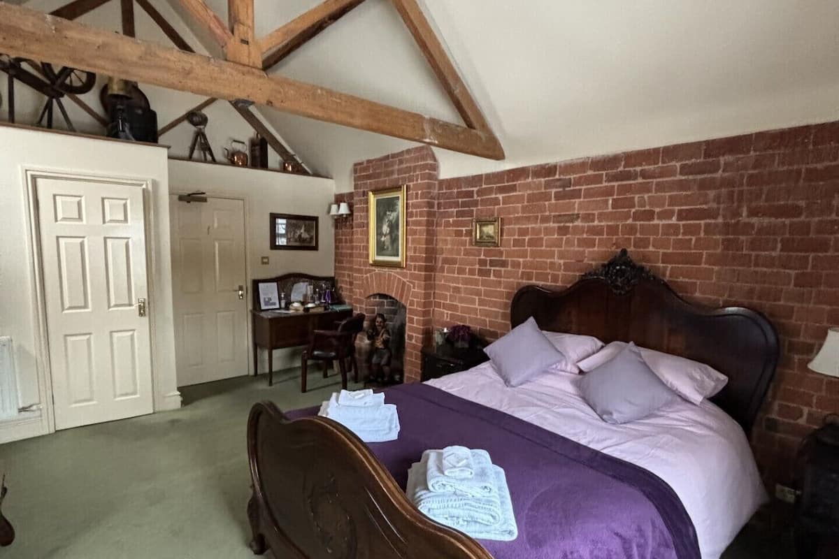A bedroom with a wooden bed, a brick wall, and a high ceiling with exposed beams.