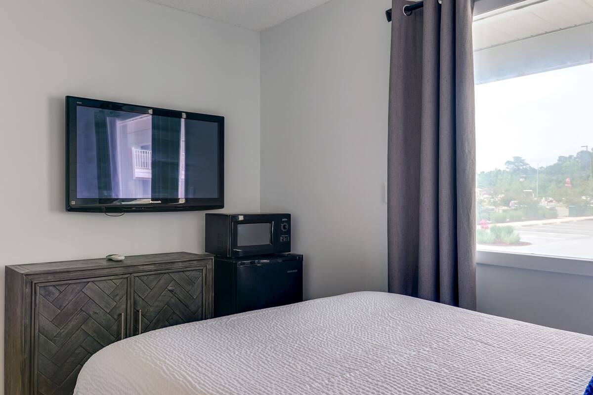 A hotel room with a bed, a TV mounted on the wall, a microwave, and a small cabinet.