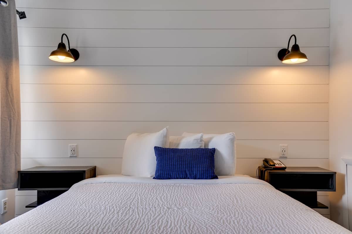 A neatly arranged hotel room with a large bed, two bedside tables, a blue patterned pillow, and wall-mounted lamps.