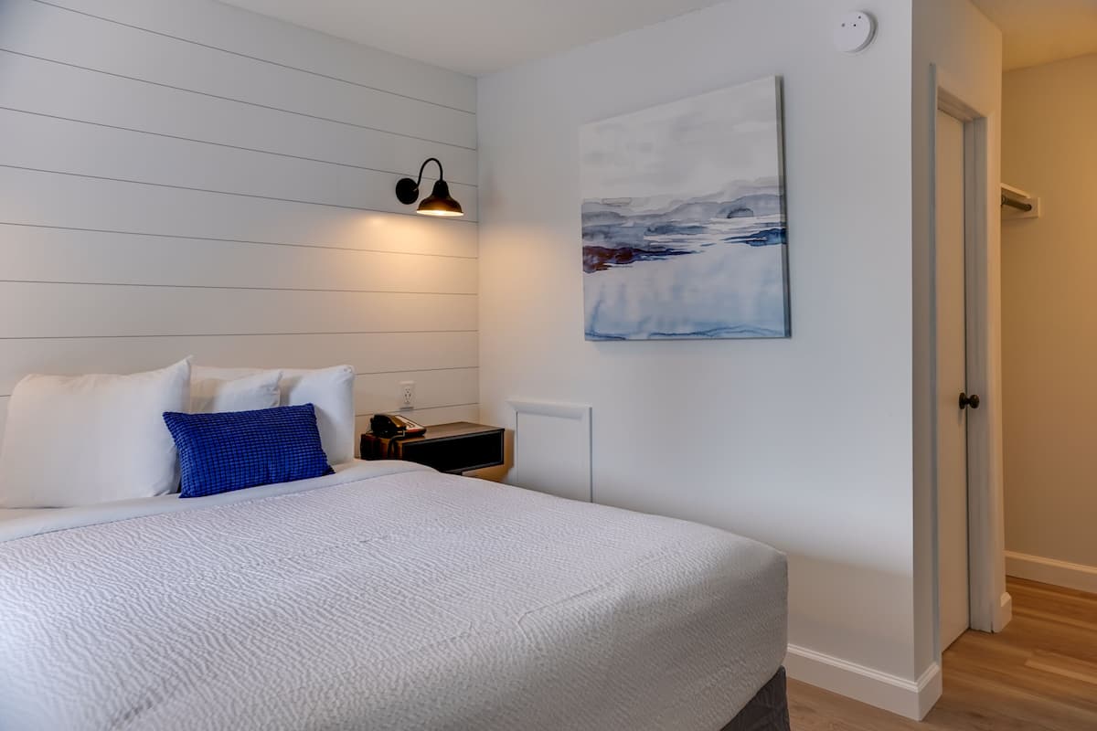 A bedroom with a bed, a nightstand, a wall-mounted lamp, and a painting.