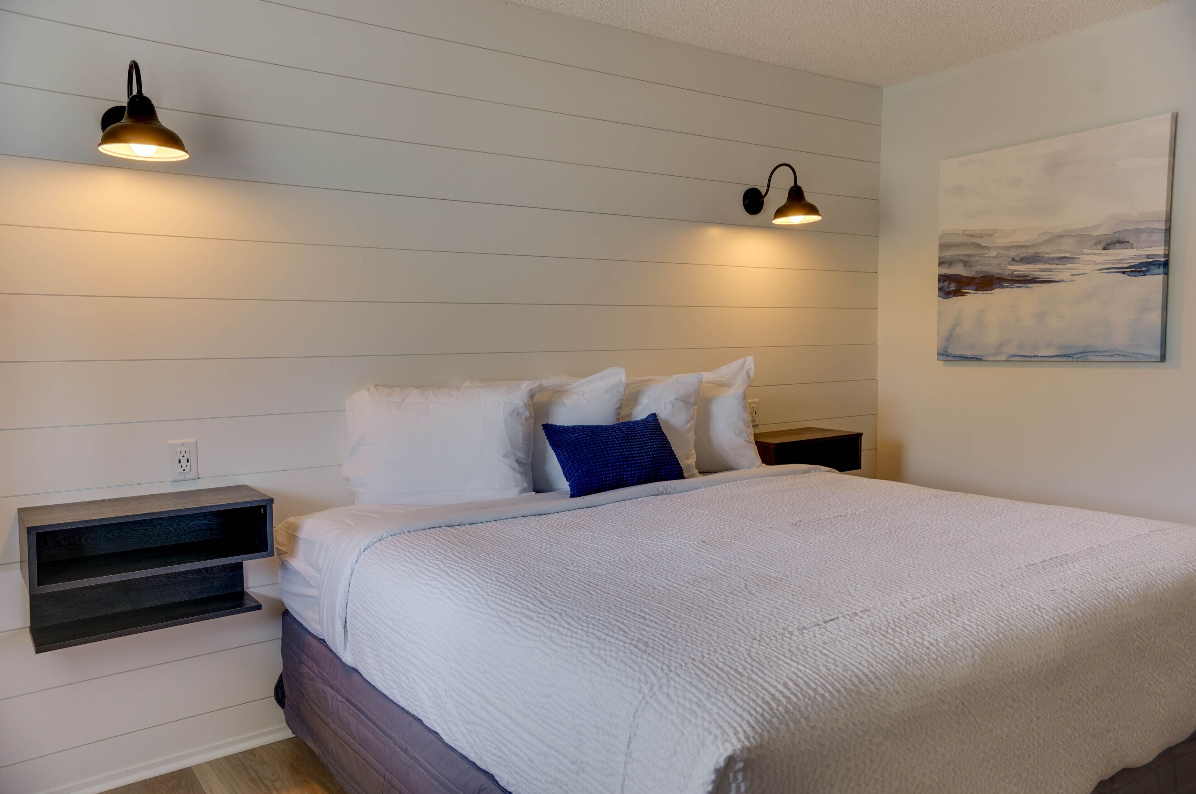 A bedroom with a bed, two wall-mounted lights, a nightstand, and a painting on the wall.