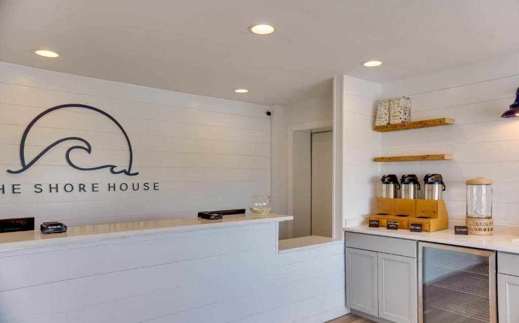A reception area with a white counter, a logo above it, and a coffee station with various items.