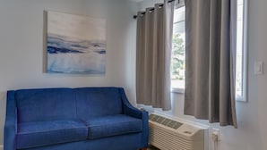 A room with a blue sofa, a painting on the wall, and a window with curtains. - The Shore House (Ocean City)