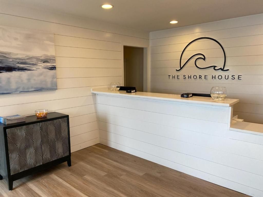 A reception area with a white reception desk, a wall-mounted logo, a painting, and a patterned side table.