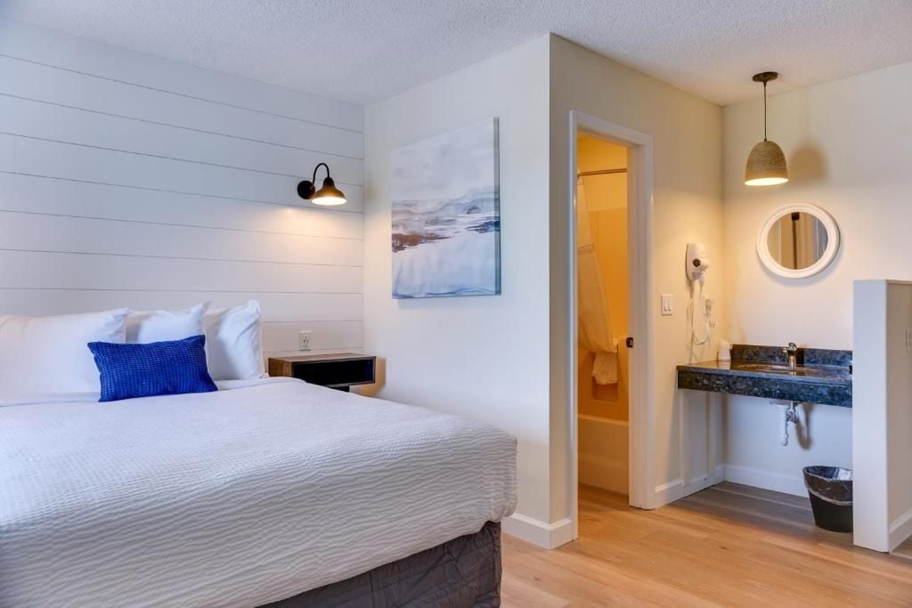 Quarto de hotel com cama, mesa de cabeceira e banheiro com pia e espelho.
