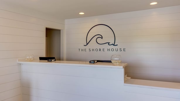 A reception desk with a logo and name "The Shore House" on the wall. - The Shore House (Ocean City)