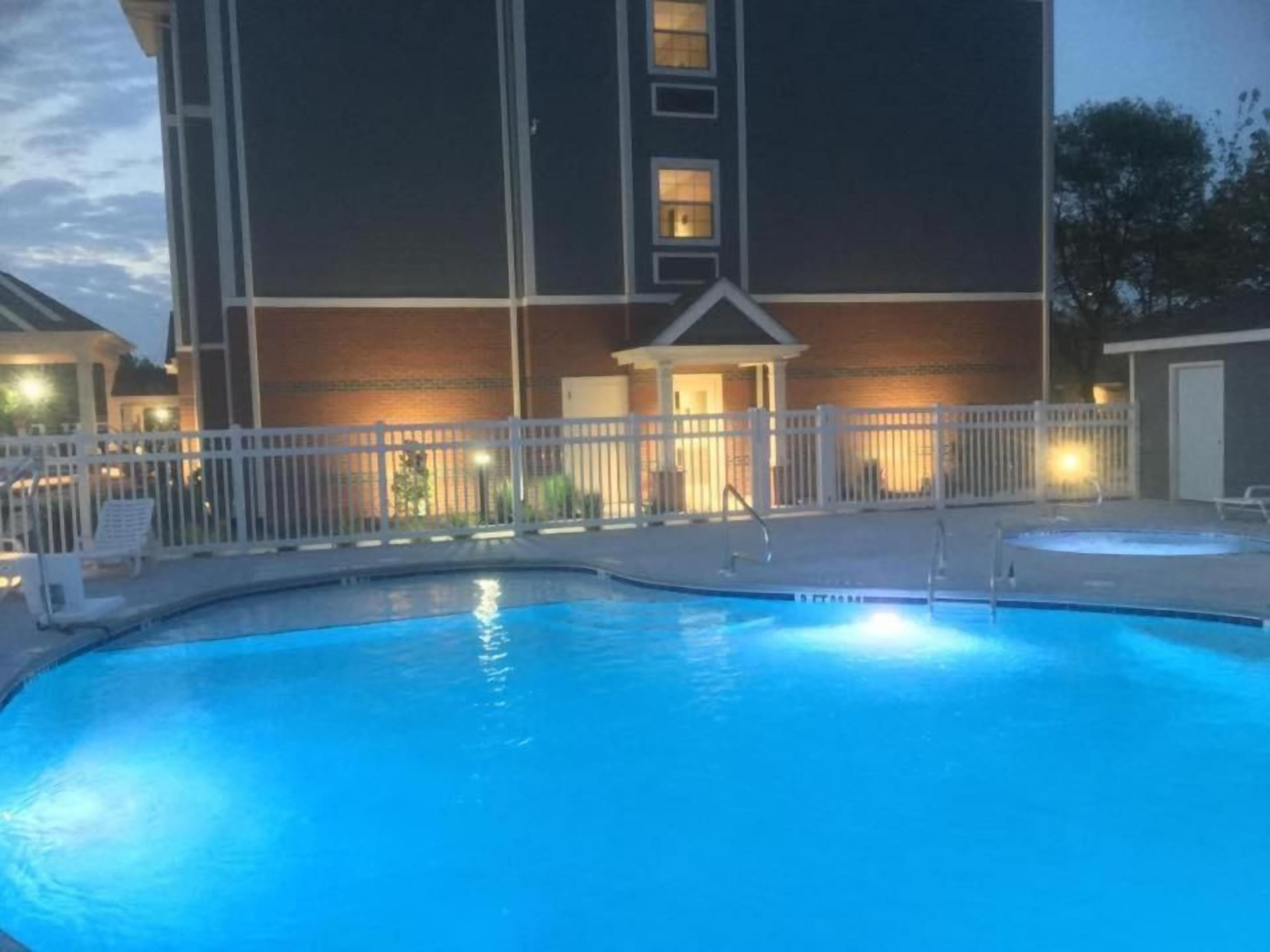 A swimming pool with a white fence and a building with a balcony in the background.