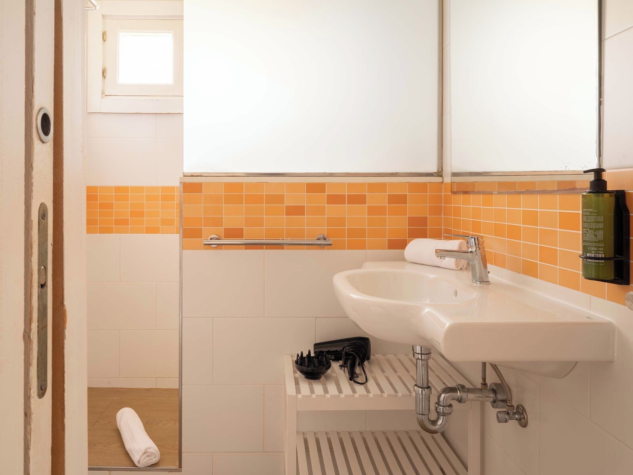 Un baño con lavamanos blanco, espejo y pared con azulejos anaranjados.