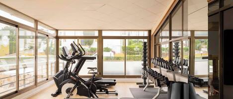 A gym with cardio equipment, weight benches, and large windows.