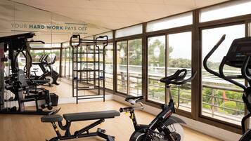 A gym with various exercise equipment, large windows, and a sign stating 'YOUR HARD WORK PAYS OFF'.