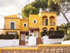 Un edificio amarillo con varios balcones, un muro de piedra en primer plano y una escalera que lleva a la entrada.