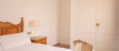 A bedroom with a wooden headboard, a bedside table with a lamp, a bed with white bedding, and a wardrobe with two doors.